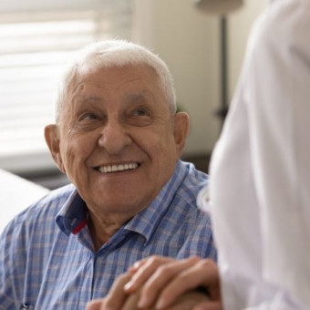 Hombre de tercera edad sonríe al tomar la mano de su cuidadora