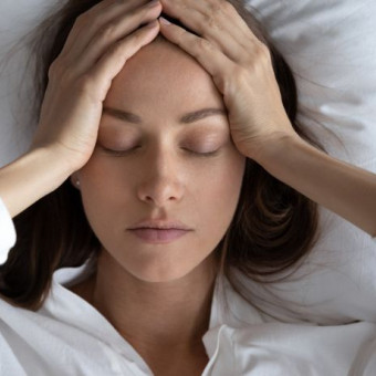 Mujer acostada en su cama se toma la cabeza como expresión de preocupación