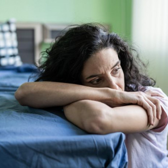 Mujer agachada al borde de su cama denota miedo y tristeza