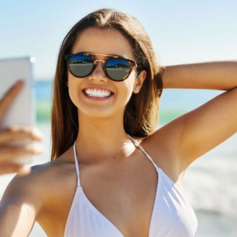 Mujer se toma fotos en la playa con vestido de baño y gafas de sol