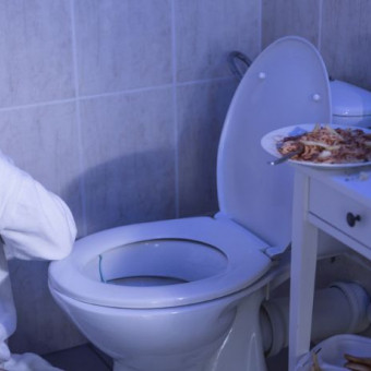 Mujer sentada en su baño cerca al sanitario con comida dentro